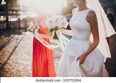 Gorgeous Bride Walking With Bridesmaids, Holding Stylish Bouquets In Warm Evening Light In Summer Street. Beautiful Happy Bride With Maid Of Honor Walking Together