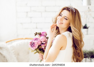 Gorgeous Bride With Wedding Bouquet Makeup And Hairstyle In Bridal Dress At Home Waiting For Groom.