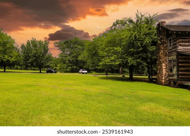 A gorgeous brown log cabin in the park surrounded by lush green grass and trees with red sky and powerful clouds at McIntosh Reserve Park in Whitesburg Georgia USA	 - Powered by Shutterstock