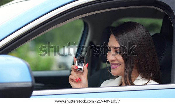 Gorgeous businesswoman driver shows key to blue\
car smiling. Well-cared woman enjoys having nice new car with black\
leather cabin closeup