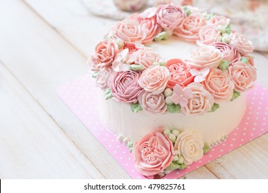 Gorgeous cake covered in roses made of butter cream icing on white wooden background