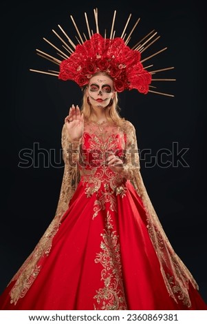 Gorgeous Calavera Catrina in a festive rich red dress and headdress stands with fire on her hands on a black background. Sugar skull girl. Day of The Dead. Halloween. Santa Muerte. Dia de los Muertos.