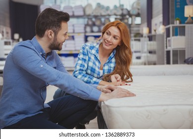 Gorgeous Cheerful Woman Laughing, Talking To Her Husband While Examining Orthopedic Mattress On Sale At Furnishings Store, Copy Space. Couple Buying New Bed Together