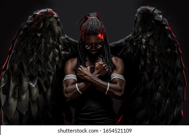 gorgeous and fantastic dark angel having big black wings, african male with strong body stand in the flesh of angel, white strips on muscular hands and dreadlocks on head. isolated photoshot