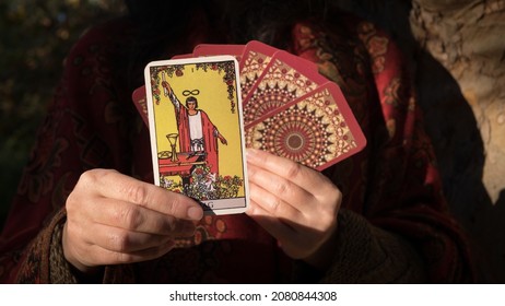 Gorgeous female hand holds a tarot card THE MAGICIAN close-up. Willpower, creation, manifestation, illusions. Fortune teller dressed in bohemian style holds a tarot card with the sign of the magician. - Shutterstock ID 2080844308