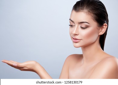 Gorgeous Girl With Dark Wet Hair And Nude Make Up And Naked Shoulders At Studio Background, SPA Concept, Close Up Portrait, Holding Product.