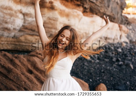 Gorgeous girl in a long white dress on the ocean at the beach. The model is inherited by nature laughing, having fun, going crazy. Happy girl on vacation, summer, emotions. The bride on vacation.