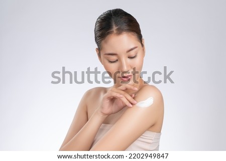 Gorgeous girl with soft makeup applying moisturizing skincare cream on shoulder isolated over white background. Skincare cream applied by female model concept.