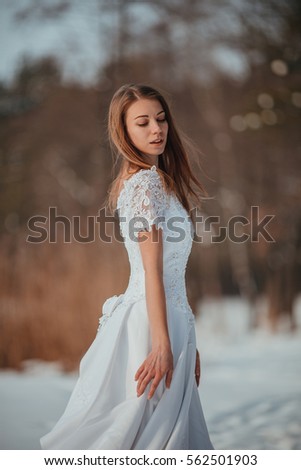Gorgeous girl in vintage white wedding dress walking in winter forest. Cold winter sun. 