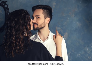 Gorgeous Glamour Couple Hugs And Kissing. Elegant Man With Trendy Beard And Smirk Face. Handsome Male With Confident Look And Stylish Hairstyle In Old Appartment Photostudio Room.
