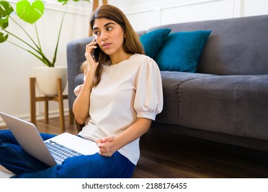 Gorgeous hispanic woman using her laptop and talking on the phone with a client while working from home 