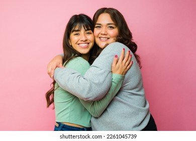 Gorgeous hispanic women best friends hugging sharing love looking at the camera on a pink background - Shutterstock ID 2261045739