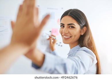 Gorgeous Indian woman in blue shirt high fiving coworkers at white board for concept about business development
