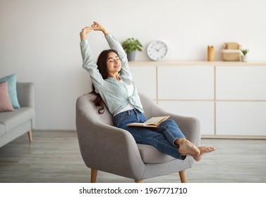 Gorgeous Indian woman stretching in comfy armchair while reading indoors. Attractive young lady with open book, enjoying lazy morning, having peaceful weekend. Stay home hobbies - Shutterstock ID 1967771710