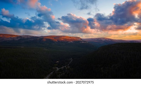 Gorgeous landscape aerial view of a canyon in the beautiful Uinta Wasatch Cache National Forest in Utah with a highway below surrounded by pine trees and rocky mountains during a vivid summer sunset.