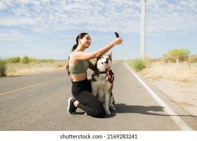 Gorgeous latin woman smiling while taking a selfie with his husky dog while exercising outdoors