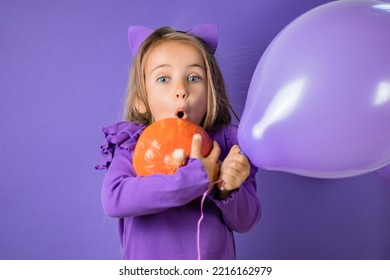 Gorgeous little girl with cat ears, balloons and a pumpkin in her hand on a purple background, Halloween concept - Shutterstock ID 2216162979