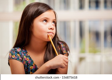 Gorgeous Little Girl Looking Up Toward Copy Space And Thinking While Holding A Pencil Near Her Mouth