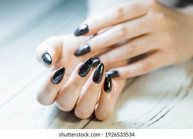Gorgeous manicure, black nail polish with sequins, close-up photo. Women's hands on a simple background.