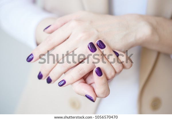 Gorgeous manicure, dark purple tender color nail\
polish, closeup photo. Female hands over simple background of\
casual clothes