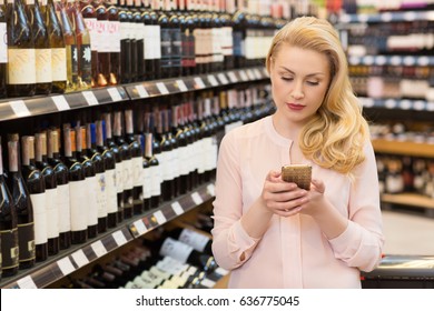 Gorgeous Mature Blonde Woman Using Her Mobile Phone While Shopping At The Wine Store Copyspace Technology Mobility Internet Online Buying Winery Shop Consumerism Food Drinks Supermarket Concept