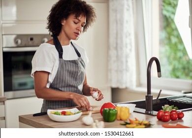 Gorgeous mixed race woman in apron standing in kitchen and peeling garlic. - Powered by Shutterstock