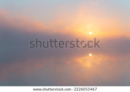 Gorgeous morning scenery with the amazing rising sun through the dense fog over the water's surface. Symmetrical reflection in calm water.