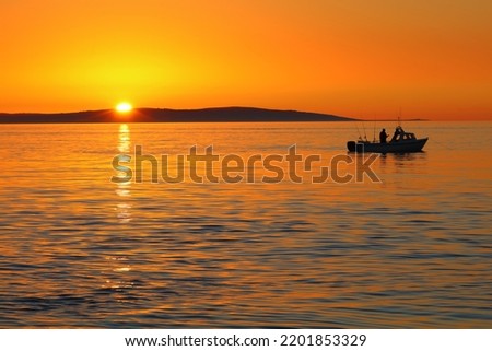 Gorgeous Orange Sunset with silhouette of small boat and Isle of Anglesey in the Background.