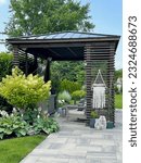 Gorgeous outdoor living backyard area with pergola  pavillion, sofa, chairs, outdoor rug,  tequila bar and stunning Techo Bloc patio pavers. Country summer, boho vibe surrounded by nature and plants.