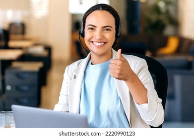 Gorgeous Positive Confident Brazilian Or Latino Woman, With Headset, Call Center Agent, Support Service Operator, Sits In The Office, Looks At Camera, Showing Thumb-up Gesture, Smiling Friendly