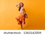 Gorgeous red-haired white woman dancing in studio. Dreamy girl in long skirt having fun on orange background.
