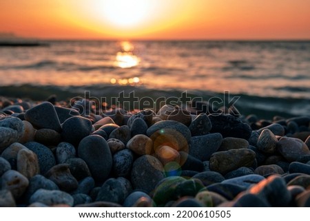 Gorgeous sea sunset landscape. MIrror reflection of dawn on wet pebble. Golden sunlight over sea waves. Close up of tide, foam and sea pebble coast