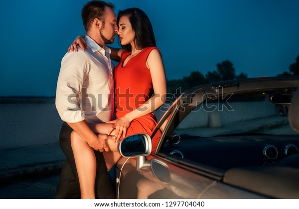 Gorgeous sexy copule of man and\
woman on a vacation car trip in summer day. Luxury grey sport car.\
Sexy fit brunette woman and man in evening outfit. Night\
portrait