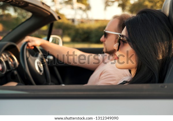 Gorgeous sexy copule of man and woman on a\
vacation car trip in summer day. Luxury grey sport car. Sexy fit\
brunette woman and man in casual outfit.\
Sunset