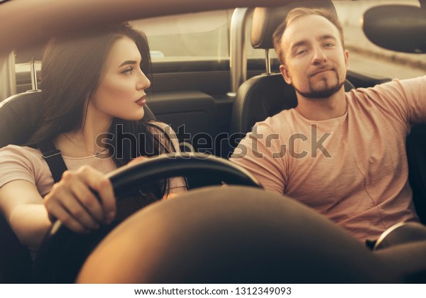 Gorgeous sexy copule of man and woman on a\
vacation car trip in summer day. Luxury grey sport car. Sexy fit\
brunette woman and man in casual outfit.\
Sunset