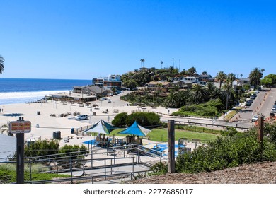 gorgeous shot of the blue ocean water, lush green palm trees and beach houses with people walking along the beach at Moonlight State Beach in Encinitas California USA