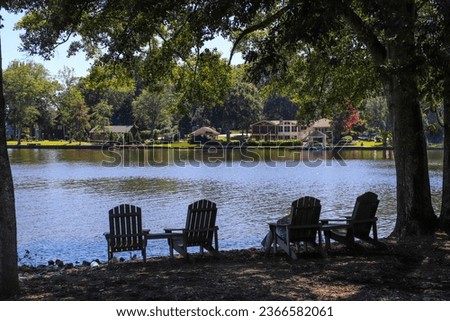 a gorgeous shot of people relaxing on the banks of the lake in lawn chairs with simmering lake water surrounded by lush green trees and green grass at Lake Peachtree in Peachtree City Georgia USA