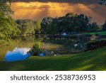 a gorgeous shot of a silky green lake surrounded by green grass and lush green and autumn colored trees and blue sky and clouds reflecting off the water at Lenox Park in Brookhaven Georgia USA	