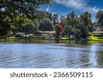 a gorgeous shot of the still blue waters of the lake with water fountain in the lake with lake front homes, lush green and autumn colored trees at Lake Peachtree in Peachtree City Georgia USA