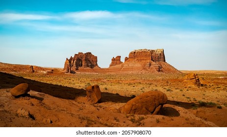 A gorgeous shot of a stunning desert plane with large rocks scattered across the ground with large red rock formations in the background on a small hike in Utah State Park, Goblin Valley.
