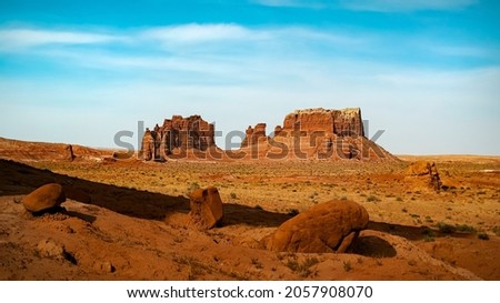 A gorgeous shot of a stunning desert plane with large rocks scattered across the ground with large red rock formations in the background on a small hike in Utah State Park, Goblin Valley.