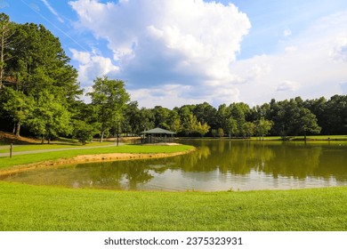 a gorgeous shot of the vast still green waters of the lake surrounded by lush green grass and trees with mallard ducks and Canadian geese, a blue pergola, blue sky and clouds at Huddleston Pond Park	 - Powered by Shutterstock