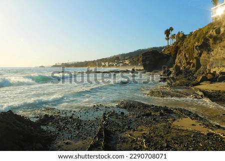 a gorgeous summer landscape at the beach with people on the shore, silky brown sand, vast blue ocean water and waves rolling into the beach at West Street Beach in Laguna Beach California USA