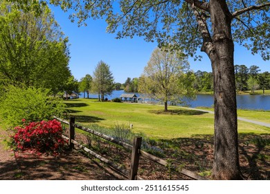 A gorgeous summer landscape in the garden with a lake and lush green trees, grass and plants, a brown wooden boathouse, red flowers, and wooden fence with blue sky at Callaway Gardens in Pine Mountain - Powered by Shutterstock