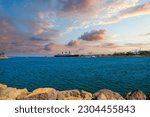 a gorgeous summer landscape at Long Beach Harbor with blue ocean water, the Queen Mary, shipping cranes and rocks along the shore and powerful clouds at sunset in Long Beach California USA