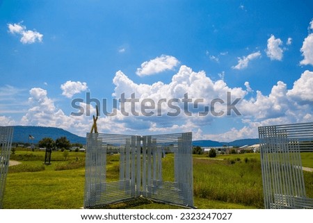 a gorgeous summer landscape in the park with sculptures and lush green trees, grass and plants with a gorgeous blue sky and powerful clouds at Sculpture Fields at Montague Park in Chattanooga