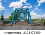 A gorgeous summer landscape at the Walnut Street Bridge with lush green trees and plants, blue sky and clouds over the Tennessee River in Chattanooga Tennessee USA