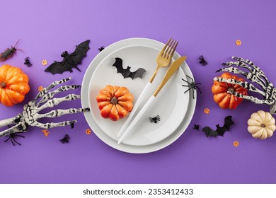 Gorgeous table setup featuring Halloween decor. Top view flat lay of plates, cutlery, halloween decorations, scary skeleton hands, orange pumpkins, confetti on purple background