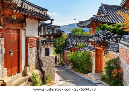 Gorgeous view of cozy old narrow street and traditional Korean houses of Bukchon Hanok Village in Seoul, South Korea. Seoul Tower on Namsan Mountain is visible on blue sky background. Scenic cityscape