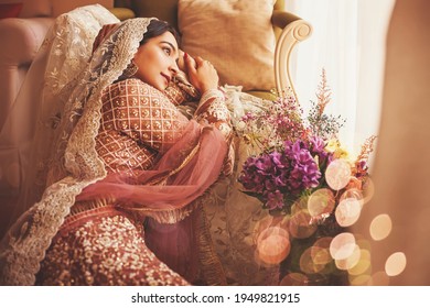 Indische Braut im Stil eines Jahrgangs, die in einem luxuriösen Hotelzimmer sitzt und traditionelle Lehenga mit Ghungat trägt 